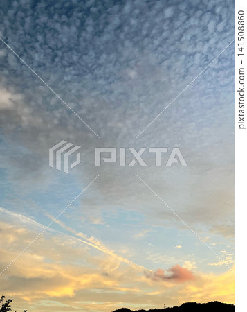 Cirrocumulus clouds spread across the sunset sky, with faint contrails remaining. Cirrocumulus clouds spread across the sunset sky, with faint contrails remaining. 141508860