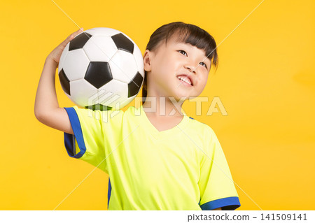 The smiling young girl leans slightly to the side on the yellow background, balancing the soccer ball casually behind her head with one hand, looking up playfully with a joyful expression in her eyes. The smiling young girl leans slightly to the side on the yellow background, balancing the soccer ball casually behind her head with one hand, looking up playfully with a joyful expression in her eyes. 141509141
