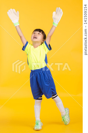 A spirited little girl wearing white goalkeeper gloves cheers with her arms raised wide towards the sky on a vibrant yellow backdrop. A spirited little girl wearing white goalkeeper gloves cheers with her arms raised wide towards the sky on a vibrant yellow backdrop. 141509154