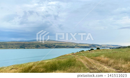 Tbilisi Sea reservoir stretches beside open grassland and a rural shoreline under layered clouds, supporting travel promotion Tbilisi Sea reservoir stretches beside open grassland and a rural shoreline under layered clouds, supporting travel promotion 141511023