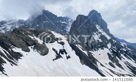Clouds drift around Chaukhi Mountain above its pass in Georgia, where steep rock towers and persistent snow illustrate alpine weather Clouds drift around Chaukhi Mountain above its pass in Georgia, where steep rock towers and persistent snow illustrate alpine weather 141511080