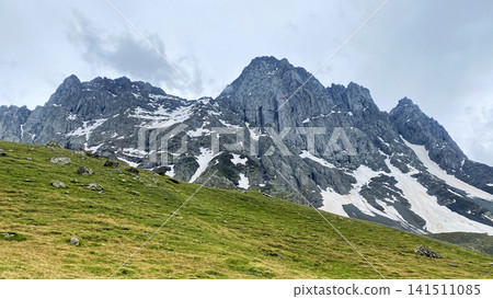 Chaukhi Mountain towers above grassy highlands and persistent snowfields in Georgia, providing a reference for climbing expeditions Chaukhi Mountain towers above grassy highlands and persistent snowfields in Georgia, providing a reference for climbing expeditions 141511085