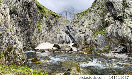 Snowmelt waterfall cuts through a rocky gorge below Chaukhi Mountain in Georgia, highlighting seasonal runoff Snowmelt waterfall cuts through a rocky gorge below Chaukhi Mountain in Georgia, highlighting seasonal runoff 141511087