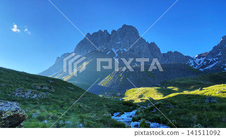 Chaukhi Mountain rises above a snow-fed stream and alpine grassland in Georgia's Greater Caucasus, presenting rugged geology Chaukhi Mountain rises above a snow-fed stream and alpine grassland in Georgia's Greater Caucasus, presenting rugged geology 141511092