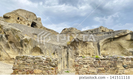 Rock-hewn facades of Uplistsikhe rise above ancient masonry in a panoramic view of the Georgian archaeological complex Rock-hewn facades of Uplistsikhe rise above ancient masonry in a panoramic view of the Georgian archaeological complex 141511118