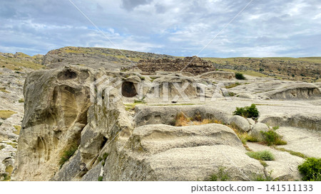 Rock-cut caves spread across Uplistsikhe in a wide ground-level view, revealing carved chambers, eroded sandstone surfaces Rock-cut caves spread across Uplistsikhe in a wide ground-level view, revealing carved chambers, eroded sandstone surfaces 141511133