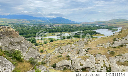 Kura River winds through a Georgian valley in a high panoramic view from Uplistsikhe, revealing rocky slopes Kura River winds through a Georgian valley in a high panoramic view from Uplistsikhe, revealing rocky slopes 141511134