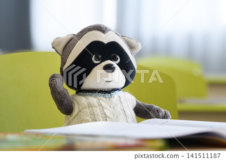 Plush Raccoon Studying at School Desk with Raised Hand. Plush Raccoon Studying at School Desk with Raised Hand. 141511187