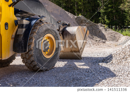 Wheel loader tire and bucket beside gravel piles at a mountain work site Wheel loader tire and bucket beside gravel piles at a mountain work site 141511336