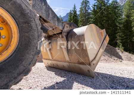 Steel loader bucket and heavy tire in a low mountain construction close-up Steel loader bucket and heavy tire in a low mountain construction close-up 141511341
