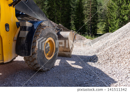Wheel loader beside a long gravel stockpile on a mountain work lane through forest Wheel loader beside a long gravel stockpile on a mountain work lane through forest 141511342