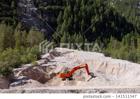 Orange tracked excavator in terraced mountain earthworks and forest clearing 141511347