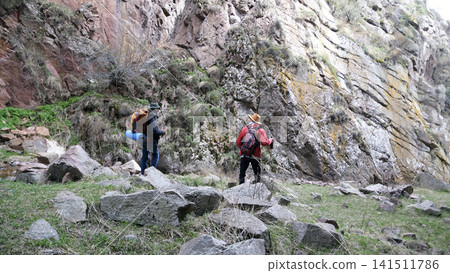 A group of two people are wandering along a high rocky mountain. Friends travel together. Tourists with backpacks went on a trip A group of two people are wandering along a high rocky mountain. Friends travel together. Tourists with backpacks went on a trip 141511786