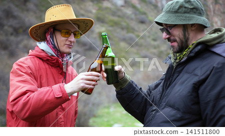 Two alcoholics are drinking in nature. Two friends are going camping. They are holding bottles of beer in their hands and having a relaxed time Two alcoholics are drinking in nature. Two friends are going camping. They are holding bottles of beer in their hands and having a relaxed time 141511800