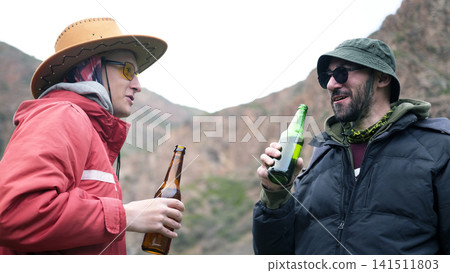 Two drunks are drinking beer in the mountains. Two male friends are chatting and holding a bottle of alcoholic beverage in their hands Two drunks are drinking beer in the mountains. Two male friends are chatting and holding a bottle of alcoholic beverage in their hands 141511803