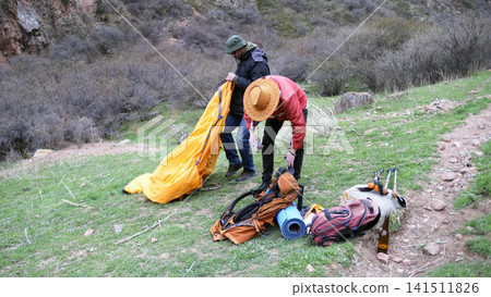 Gathering of the camp. Preparing for a new hiking day. A gay couple is building a tent. Travel, adventure, and tourism Gathering of the camp. Preparing for a new hiking day. A gay couple is building a tent. Travel, adventure, and tourism 141511826