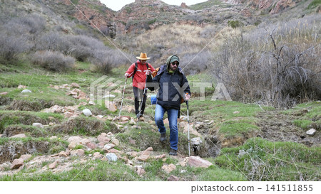 Two tourists are coming down from the mountains. Two guys are walking on rocks and grass in the wilderness 141511855