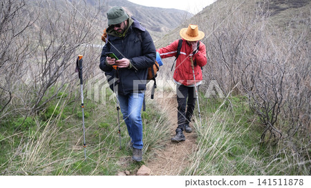 Two tired travelers stopped on the trail to look at the map of the way ahead. The guide took out his phone and checked the route Two tired travelers stopped on the trail to look at the map of the way ahead. The guide took out his phone and checked the route 141511878