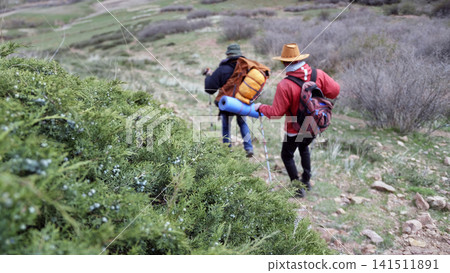Two pilgrims go to the holy places, view from the back. Travelers are walking along a dirt trail on a warm cloudy day Two pilgrims go to the holy places, view from the back. Travelers are walking along a dirt trail on a warm cloudy day 141511891