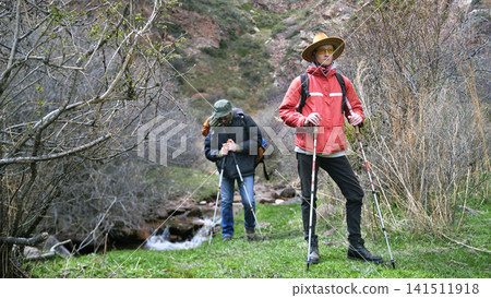 A young confident guy in a cowboy hat stands proudly and waits for his hiking companion. Two people are walking through the forest A young confident guy in a cowboy hat stands proudly and waits for his hiking companion. Two people are walking through the forest 141511918
