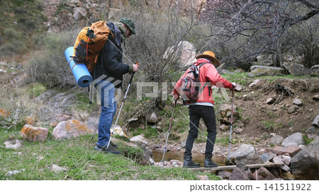 Two travelers cross a small river through a makeshift ferry. Students are walking through the forest in search of adventure Two travelers cross a small river through a makeshift ferry. Students are walking through the forest in search of adventure 141511922