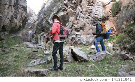 Two men are hiking in a rocky area. A group of tourists walks along the gorge looking around. The travelers are walking along a rocky path Two men are hiking in a rocky area. A group of tourists walks along the gorge looking around. The travelers are walking along a rocky path 141511941