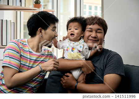 Two men comforting a crying baby on a sofa at home, showing care, affection, support, tenderness, bonding, comfort, concern, caregiving, and emotional family connection Two men comforting a crying baby on a sofa at home, showing care, affection, support, tenderness, bonding, comfort, concern, caregiving, and emotional family connection 141511996