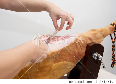Professional slicing of thin Spanish jamon slice on wooden stand 141512319