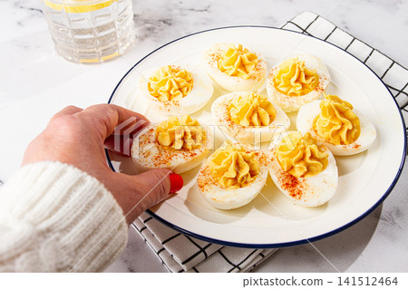 stuffed eggs with paprika, on a plate, a woman's hand reaches for it, 141512464