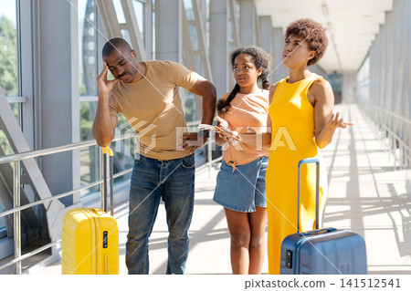 Confused black family of three at airport, father looking frustrated Confused black family of three at airport, father looking frustrated 141512541