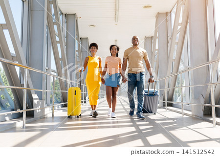 Happy Black parents and daughter walk hand in hand in airport corridor Happy Black parents and daughter walk hand in hand in airport corridor 141512542