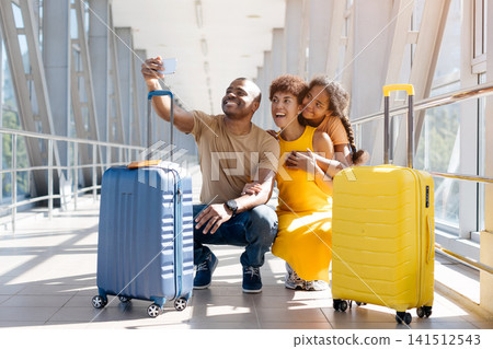 Happy Black father taking smartphone selfie with wife and daughter in airport Happy Black father taking smartphone selfie with wife and daughter in airport 141512543