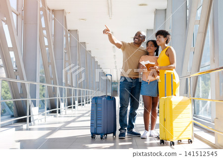 Smiling Black father pointing toward airport signs while standing with her family Smiling Black father pointing toward airport signs while standing with her family 141512545