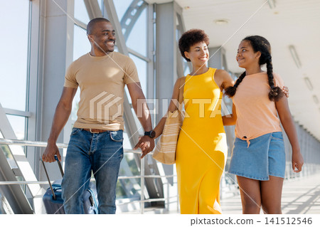 Smiling Black parents walking with their daughter through bright airport terminal Smiling Black parents walking with their daughter through bright airport terminal 141512546