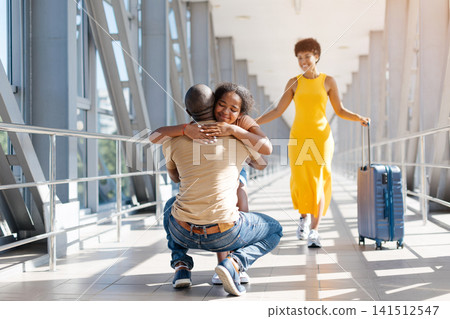 Father hugging daughter at airport walkway while African American mother approaches smiling Father hugging daughter at airport walkway while African American mother approaches smiling 141512547
