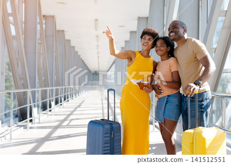 Smiling Black mother pointing toward airport signs while standing with her family Smiling Black mother pointing toward airport signs while standing with her family 141512551