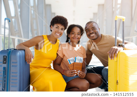 Happy Black family crouching together between rolling suitcases at bright airport terminal Happy Black family crouching together between rolling suitcases at bright airport terminal 141512555