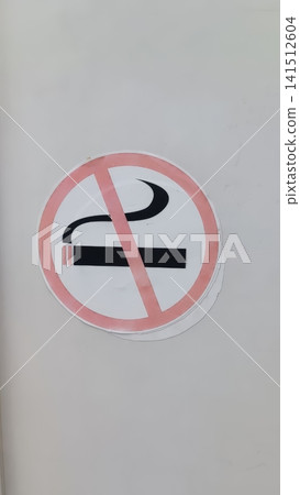 Close up of a circular No Smoking prohibition sign mounted on a plain white wall, with a bold red diagonal slash over a black cigarette and smoke lines. Close up of a circular No Smoking prohibition sign mounted on a plain white wall, with a bold red diagonal slash over a black cigarette and smoke lines. 141512604