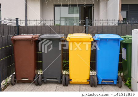 Colorful recycling bins lined up outside residential house behind fence 141512939