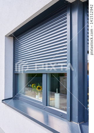 Partially lowered exterior roller shutter shades kitchen window with sunflowers and paper towel roll visible inside Partially lowered exterior roller shutter shades kitchen window with sunflowers and paper towel roll visible inside 141512942