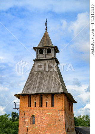 Weathered wooden tower rises above red brick base. Cloudy sky frames ancient structure. Rustic charm evokes historic village spirit. Vertical lines suggest aged craftsmanship Weathered wooden tower rises above red brick base. Cloudy sky frames ancient structure. Rustic charm evokes historic village spirit. Vertical lines suggest aged craftsmanship 141513139