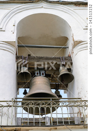 Large bell hangs within an arched stone bell tower. Smaller bells rest above, suspended from wooden beams. White pillars frame the bell chamber structure. Metal railing protects the bells below Large bell hangs within an arched stone bell tower. Smaller bells rest above, suspended from wooden beams. White pillars frame the bell chamber structure. Metal railing protects the bells below 141513152