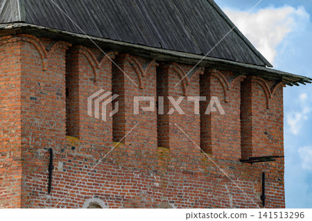 Red brick tower with arched openings and tiled roof. Weathered surface shows age and natural patina. Blue sky with soft clouds forms a serene backdrop. Detail captures architectural craftsmanship Red brick tower with arched openings and tiled roof. Weathered surface shows age and natural patina. Blue sky with soft clouds forms a serene backdrop. Detail captures architectural craftsmanship 141513296