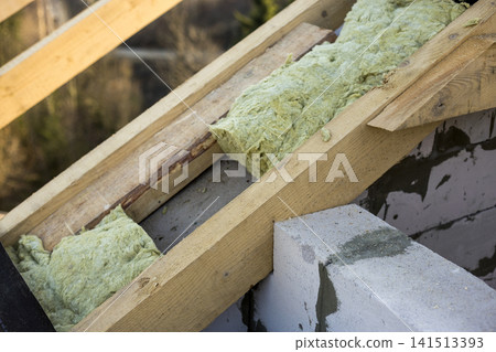 Roof construction and insulation with mineral wool. Wooden beams frame on walls of hollow foam insulation blocks. Roofing underlayment, water-resistant waterproof barrier material as protection. Roof construction and insulation with mineral wool. Wooden beams frame on walls of hollow foam insulation blocks. Roofing underlayment, water-resistant waterproof barrier material as protection. 141513393