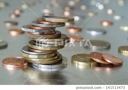 Pile of shiny coins different sizes and colors stacked unevenly on each other on colorful blurred blue abstract background. Money saving and financial risk concept. Pile of shiny coins different sizes and colors stacked unevenly on each other on colorful blurred blue abstract background. Money saving and financial risk concept. 141513473