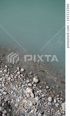 High-angle photograph of rocky shoreline meeting turquoise-blue rippled water, coastal concept. High-angle photograph of rocky shoreline meeting turquoise-blue rippled water, coastal concept. 141513560