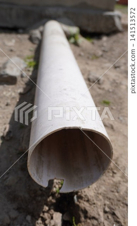 Close-up photograph of a white PVC pipe lying horizontally on dusty ground with a shadow, utility concept. Close-up photograph of a white PVC pipe lying horizontally on dusty ground with a shadow, utility concept. 141513572