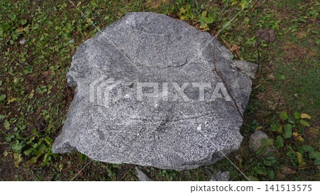 Large gray granite boulder with rough texture sitting on short green grass and soil, stability concept. Large gray granite boulder with rough texture sitting on short green grass and soil, stability concept. 141513575