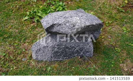 Large gray granite boulder split in two on green grass with yellow patches, natural concept. Large gray granite boulder split in two on green grass with yellow patches, natural concept. 141513589
