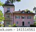 Historic house with pink walls surrounded by green trees in a park 141514561
